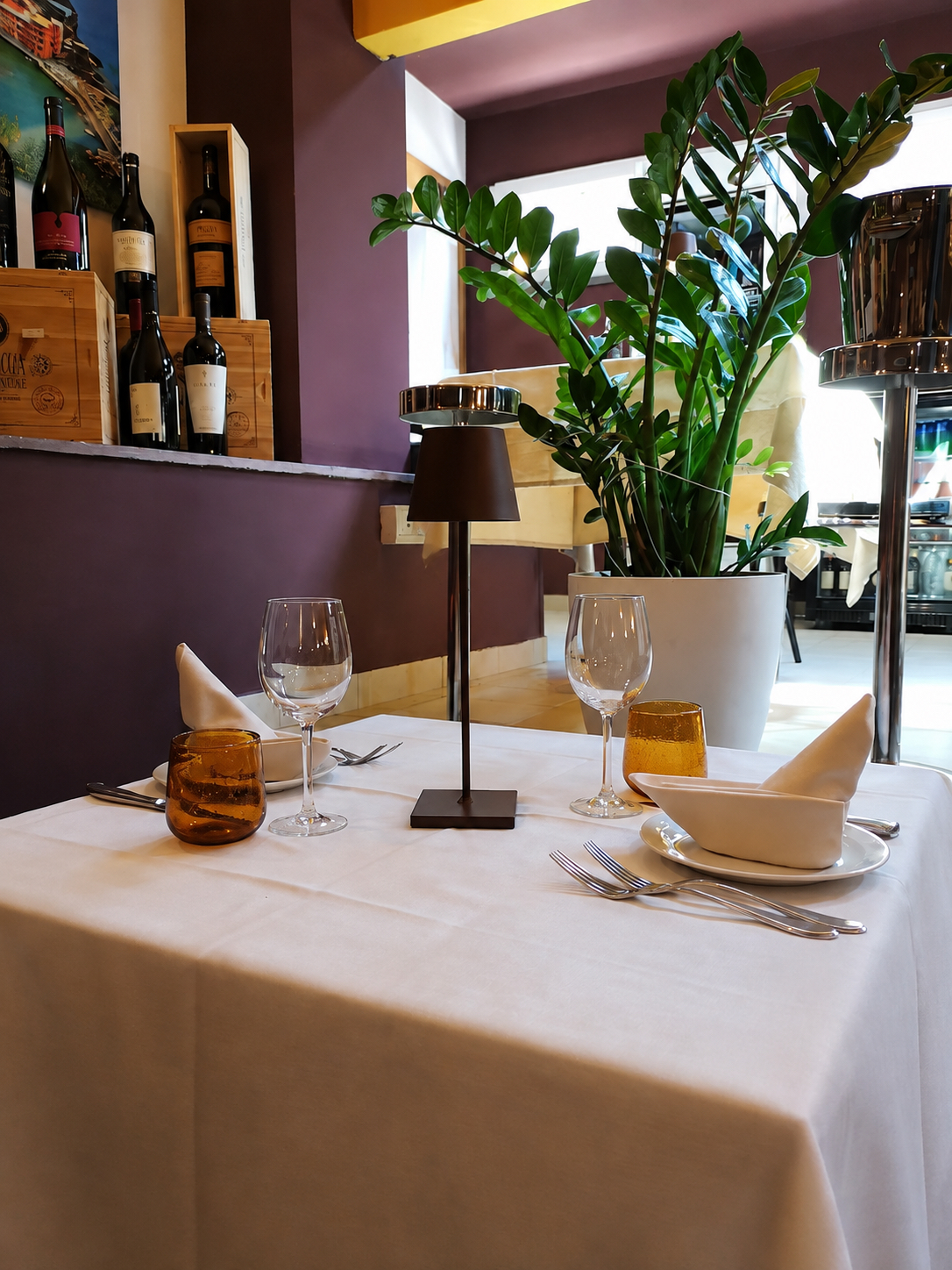 Tavolo apparecchiato de La Taverna con lampada, bicchieri e pianta verde