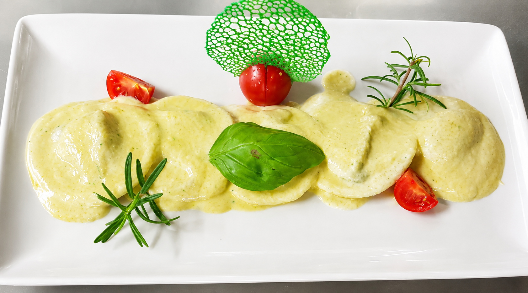 Ravioli burro e salvia con basilico, pomodorini e rosmarino serviti su piatto bianco